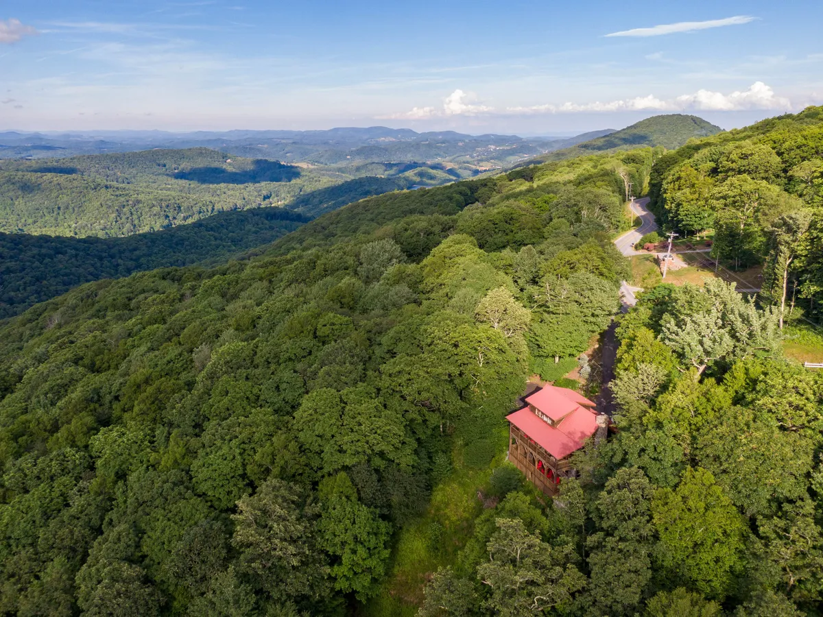 A wide view of the retreat nestled among a green forest with a stunning mountain range in the background. The home sits at the edge of the woods, highlighting its seclusion and scenic surroundings.