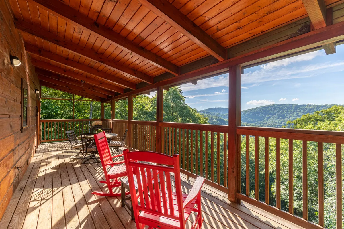 This exterior image features a deck with classic red rocking chairs overlooking a breathtaking mountain view, bordered by sturdy wooden railings. The tranquil setting invites relaxation and group conversations surrounded by nature.