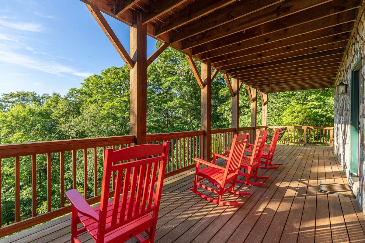 The image showcases a wooden deck with red rocking chairs, surrounded by lush greenery, emphasizing a peaceful and inviting atmosphere. The vantage point suggests a space ideal for both quiet moments and lively gatherings.