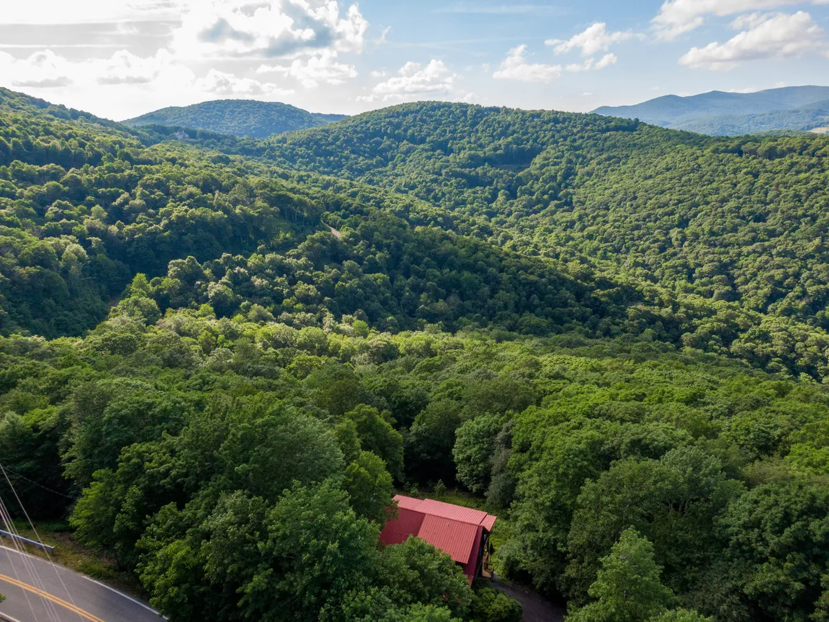 A sweeping view of lush green mountains, with a red-roofed building and a winding road snaking through the landscape. The scene is open, peaceful, and evokes a sense of escape and connection to nature.