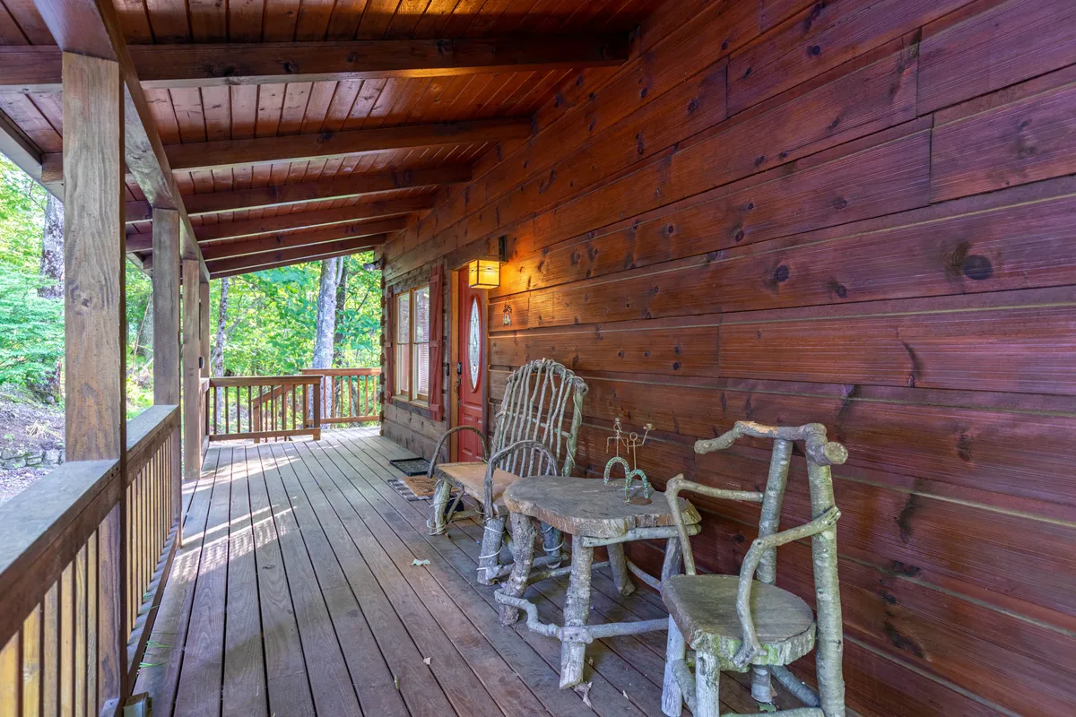 This exterior image features rustic wooden furniture on a porch, natural wood siding, and abundant greenery just outside. The inviting arrangement suggests a perfect spot for unwinding outdoors, reading, or sharing a drink while immersed in the natural surroundings.