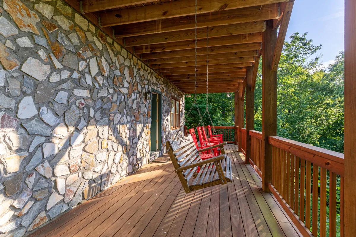 This image captures a tranquil porch scene with stone walls, swinging chairs, a wooden railing, and lush greenery all around. The cozy outdoor seating invites guests to relax, take in the surrounding nature, and unwind, setting the tone for a peaceful retreat.